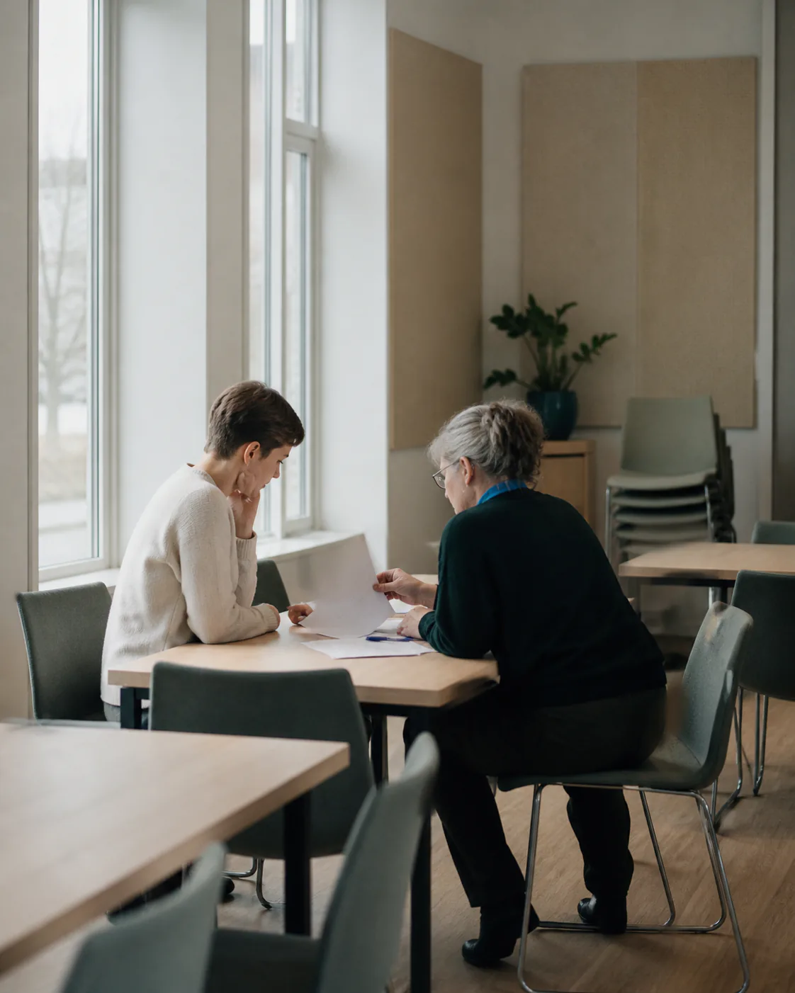 Two volunteers review unbranded papers together at a table in a modest community room.