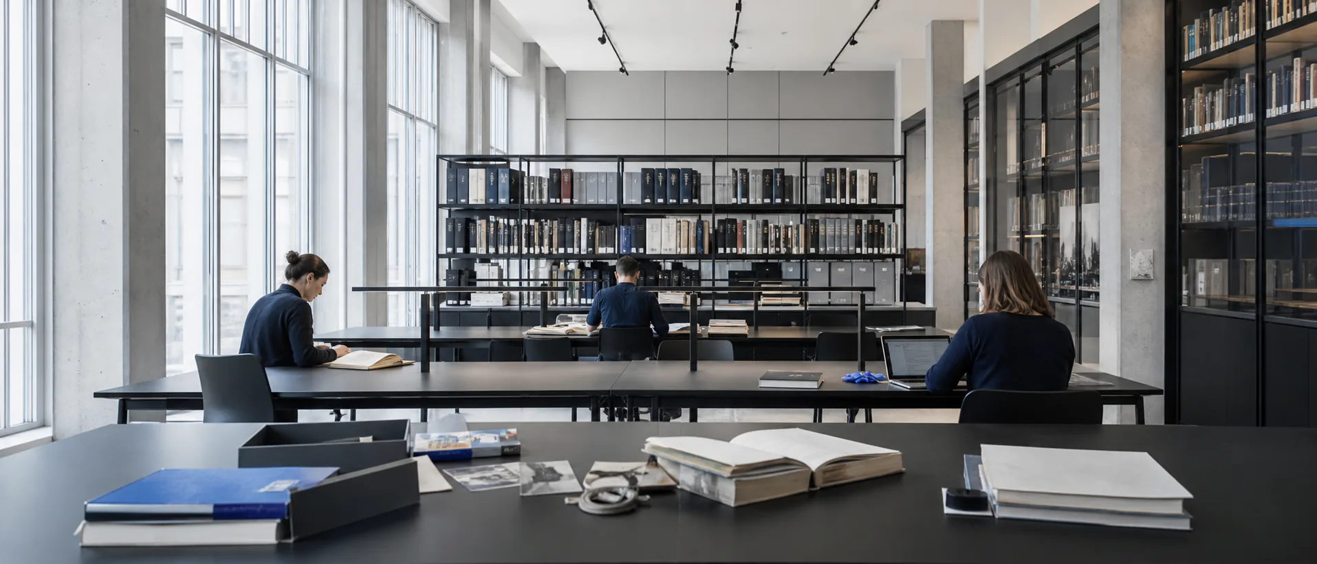 Researchers read at long tables in a calm contemporary archive and research library.
