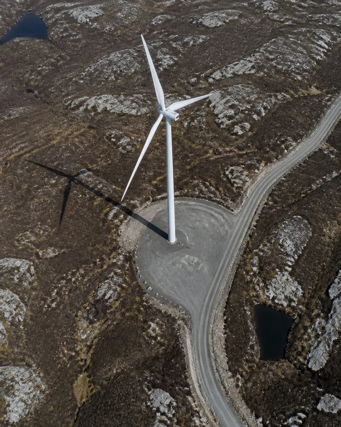 An aerial view of a wind turbine, its access road and rocky northern terrain.