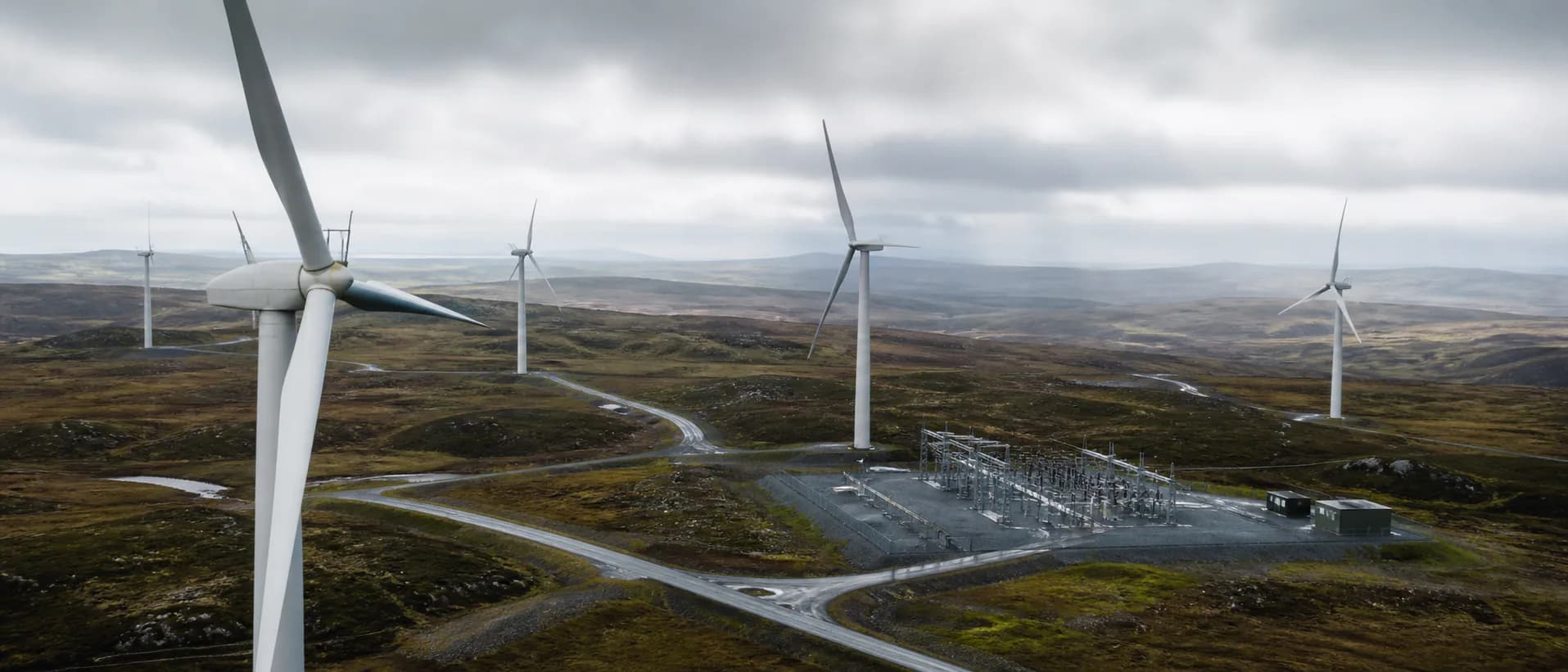 Wind turbines and an electrical substation spread across a low, rocky landscape under cloud.